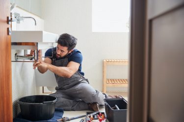 Male Plumber Working To Fix Leaking Sink In Home Bathroom