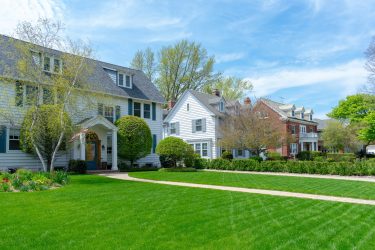 Row of traditional suburban homes with lush green front lawns in nice residential neighborhood -